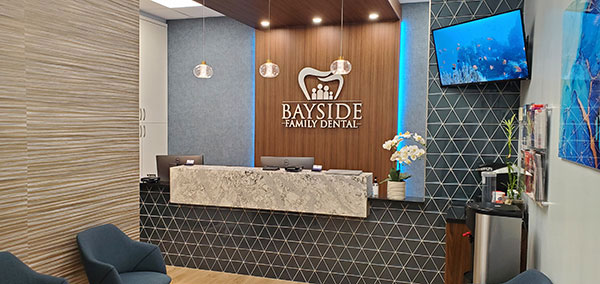 An interior view of a modern dental office waiting area with a reception desk, chairs, and decorative elements.