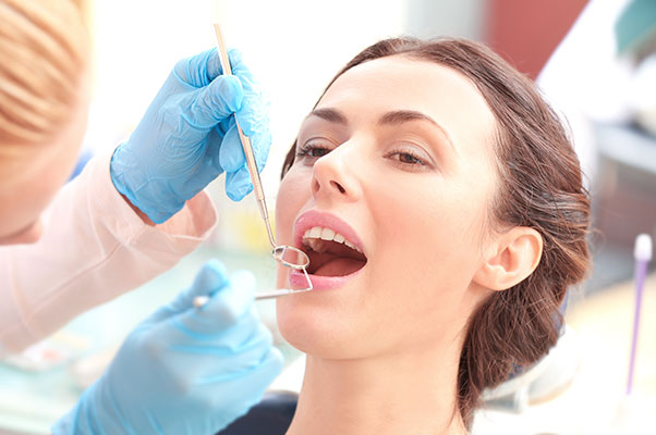 A woman receiving dental treatment from a professional in a clinical setting, with visible tools and equipment.