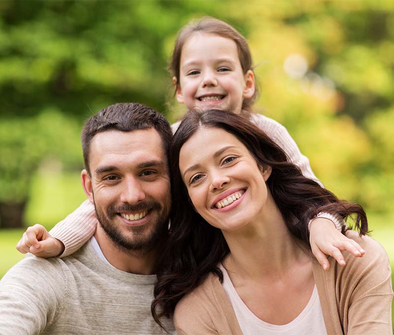 A family of four, including a man, woman, and two children, smiling together in an outdoor setting.