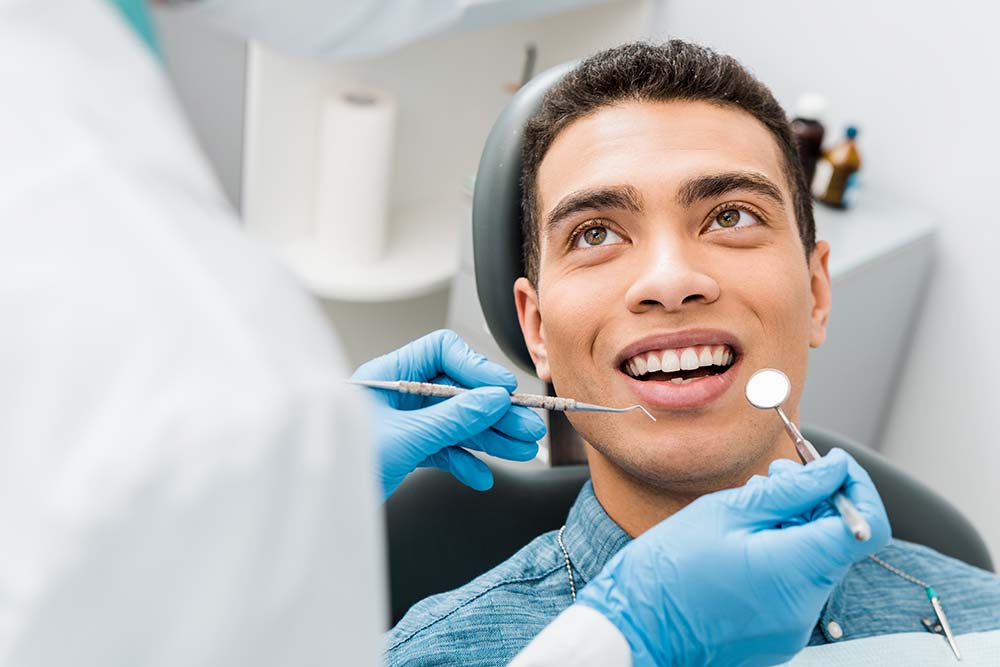 A dental professional is performing a procedure on a patient, with the patient smiling and looking towards the camera.