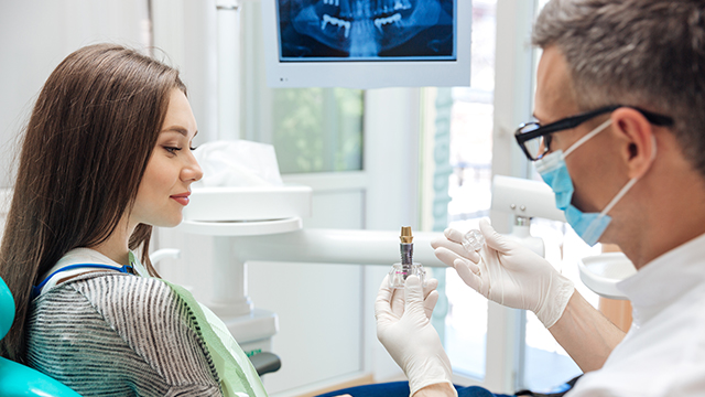 In the image, a dental professional is performing an oral examination on a patient, with both individuals wearing protective face masks and the patient seated in a dental chair.