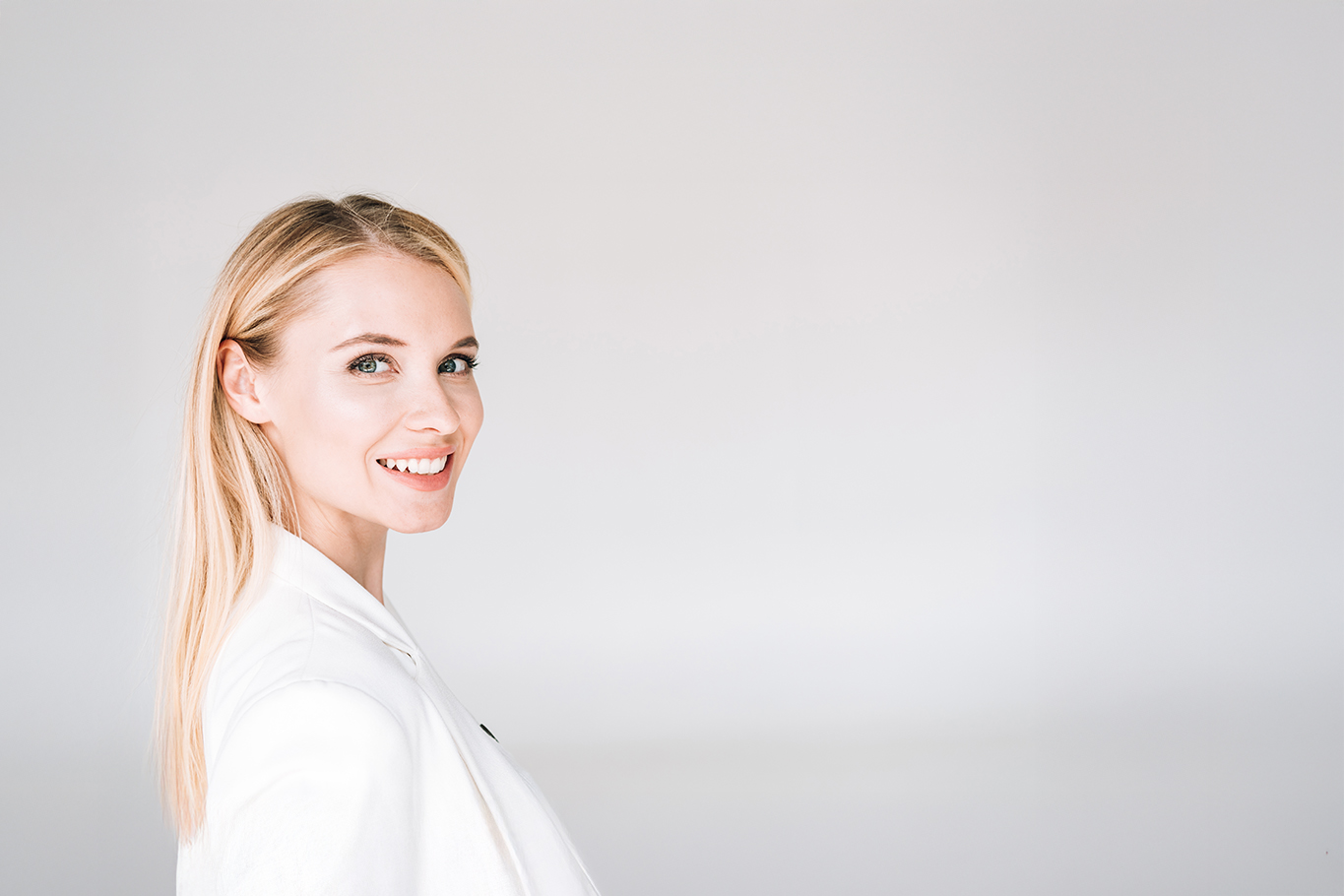 A woman with blonde hair, wearing a white top, stands against a neutral background.