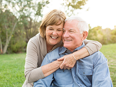 An elderly couple embracing in a warm, joyful moment, with the man wearing a blue shirt and the woman in a light-colored top.