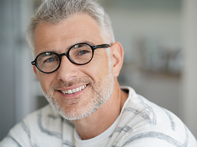 A smiling man with grey hair, wearing glasses and a white shirt, poses for the camera.