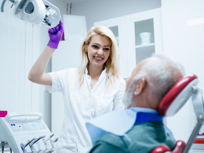 A dental professional, likely a female dentist, interacting with an older male patient in a dental office setting.