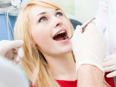 A young woman in a dental chair receiving dental treatment, with a dentist and dental assistant attending to her.