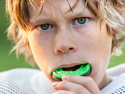 A young male athlete with blonde hair, wearing a football uniform, brushing his teeth with a green toothbrush.