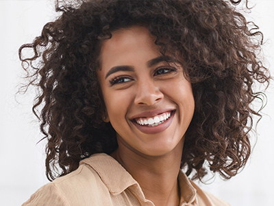 The image shows a smiling woman with curly hair, wearing a light-colored top, looking directly at the camera.